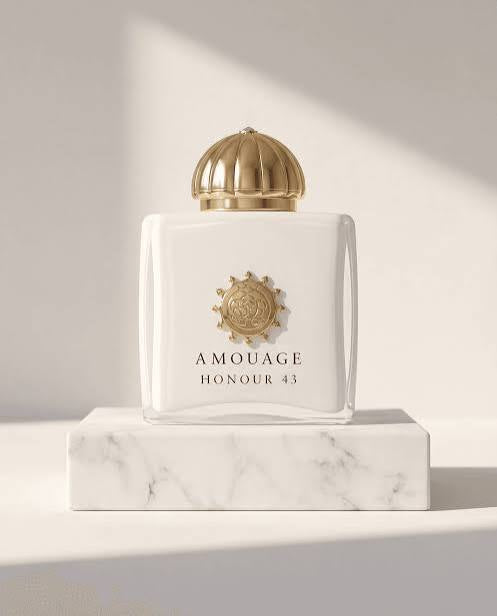 Amouage Honour 43 perfume bottle in white glass with a gold cap and gold crest, displayed on a white marble pedestal against a warm beige background with soft shadows.