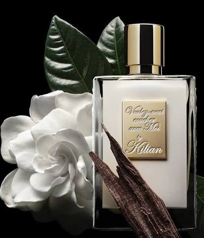 Kilian perfume bottle with white flower and vanilla bean on a black background
