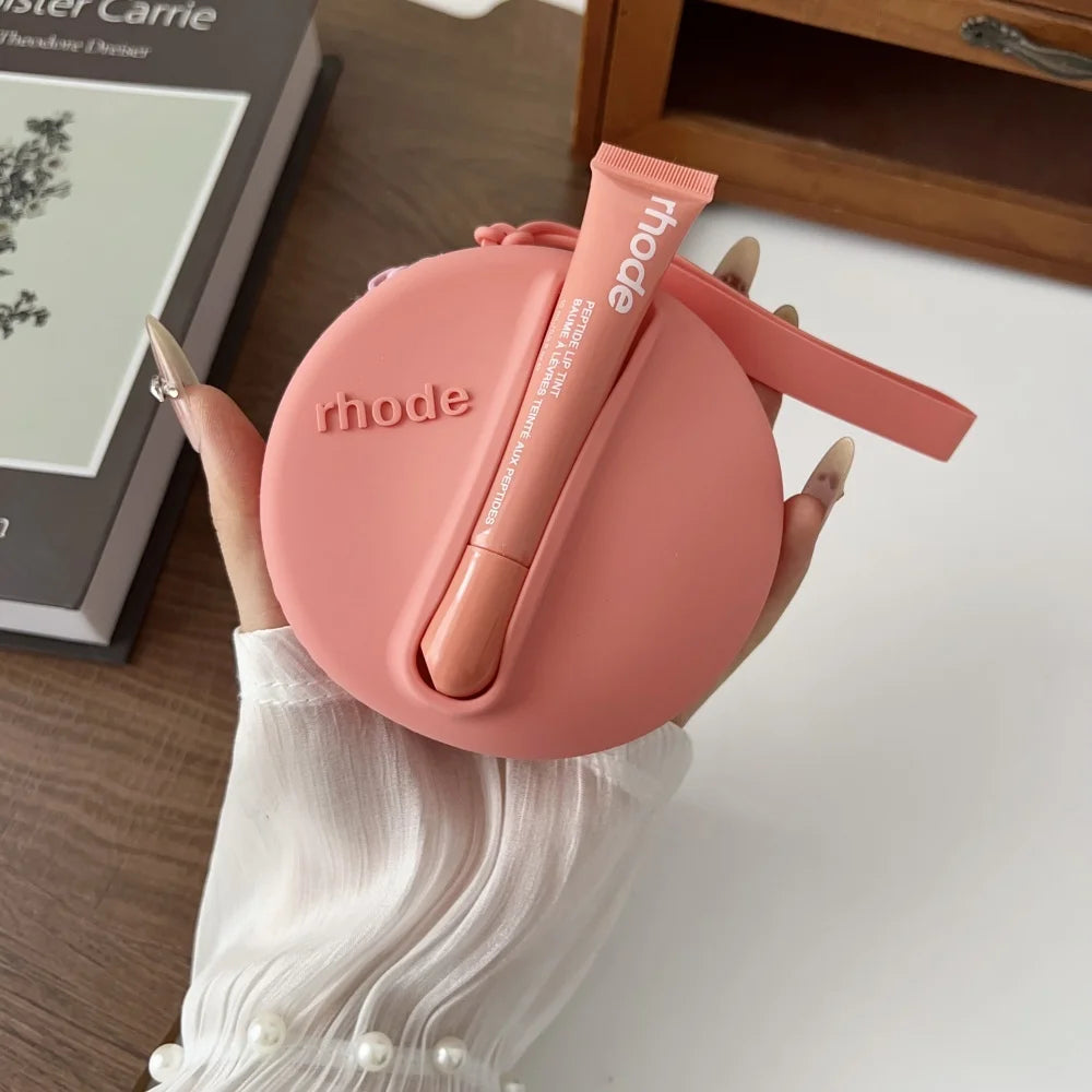 Pink lip balm case with 'rhode' branding held by a hand on a wooden surface.