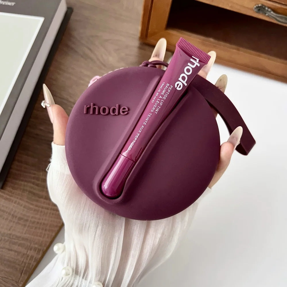 Purple case with a lip balm labeled 'rhode' held by a hand on a wooden surface.