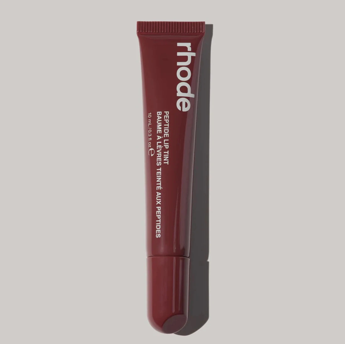 Red lip balm tube with 'rhode' branding on a beige background