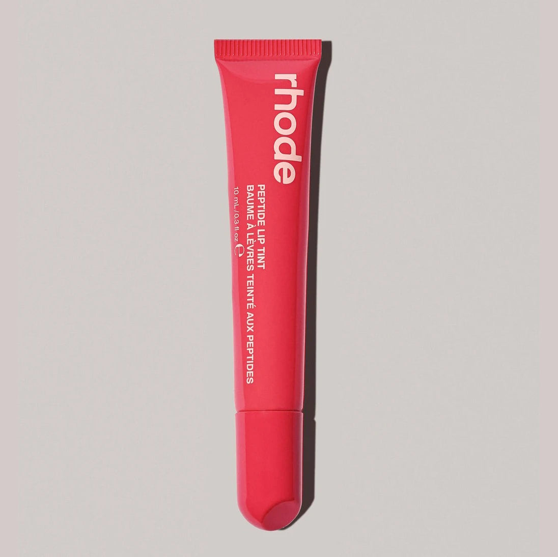 Red lip balm tube with 'rhode' branding on a gray background