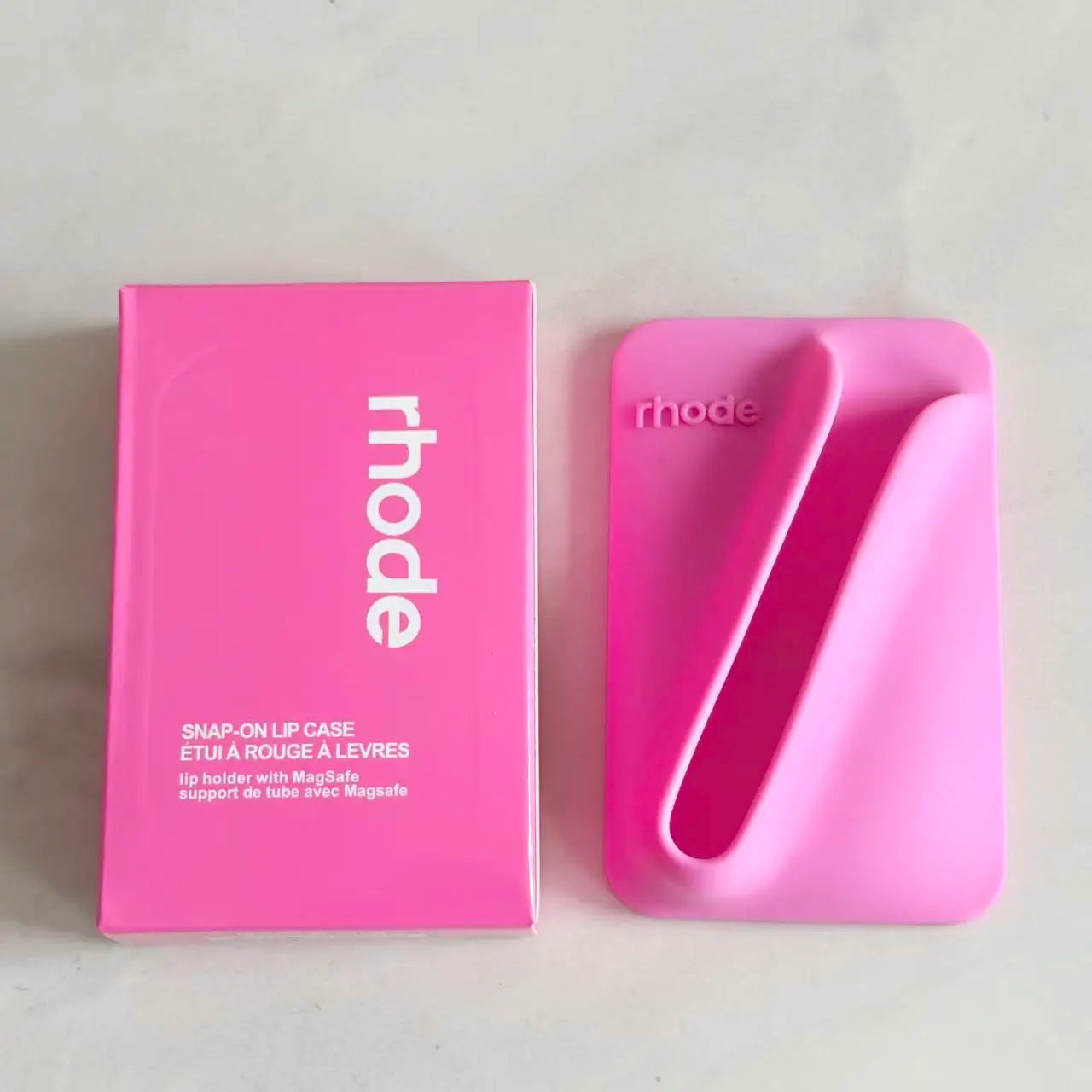 Pink 'rhode' lip care product and packaging on a light gray background